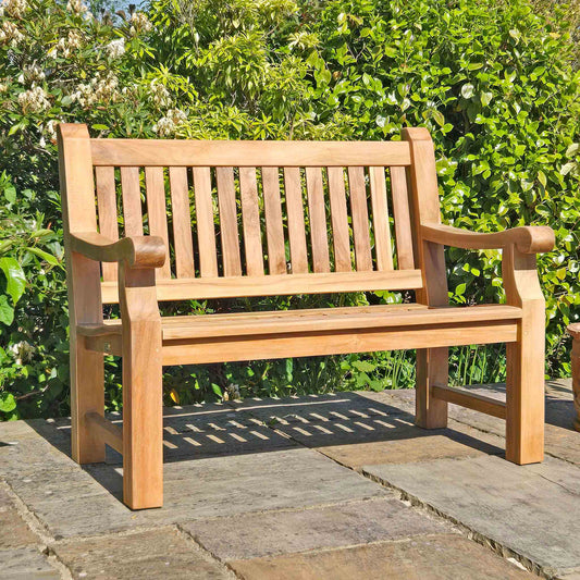 Wooden memorial bench on a stone patio with greenery in the background