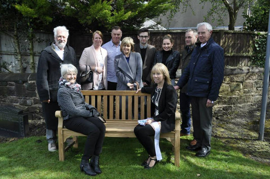 The Beatles member Stuart Sutcliffe memorial bench with friends and family sitting on it in a church grounds