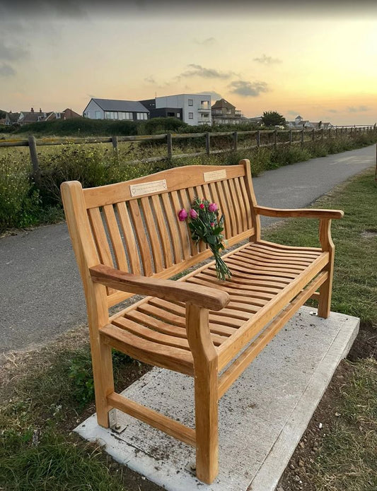A grief and remembrance memorial bench on a concrete base with flowers