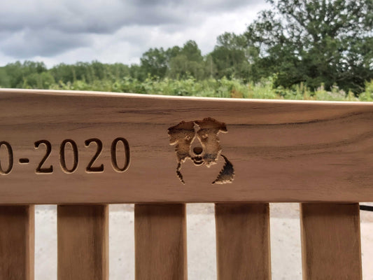 A wooden pet memorial bench engraved with a dogs head