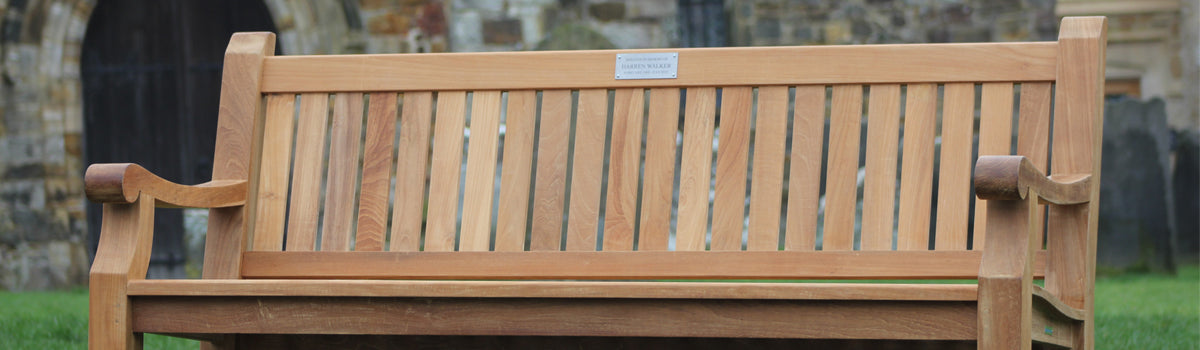 Wooden memorial bench with a plaque and a blurred background