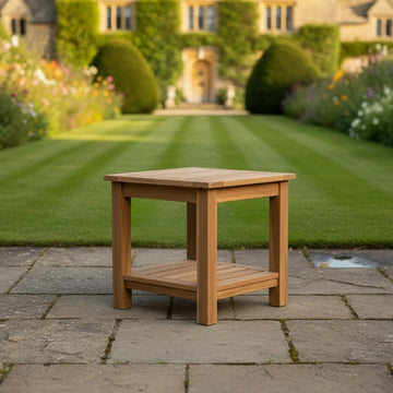 Wooden teak garden side table on a paved patio with a garden and house in the background