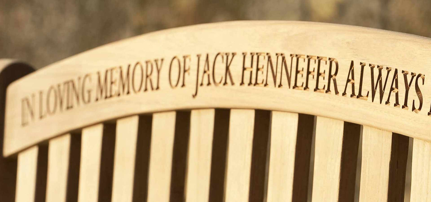 Memorial bench with engraved text 'In loving memory of Jack Hennefer always' on a blurred background