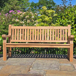 Wooden memorial bench on a stone patio with greenery in the background