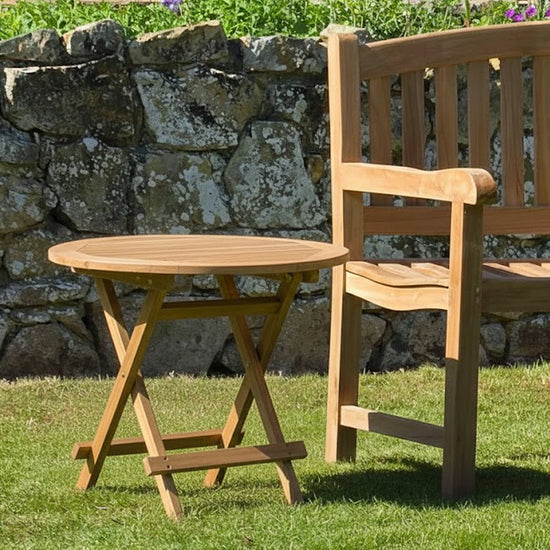 Wooden teak outdoor round folding coffee table and chair set against a stone wall and grass background