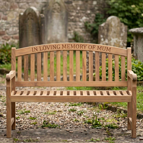Wooden teak memorial bench with 'In Loving Memory of Mum' inscription in a cemetery.