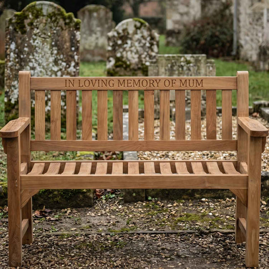 Wooden teak memorial bench with engraved text 'In Loving Memory of Mum' in a church setting.