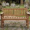 Wooden teak memorial bench with engraved text 'In Loving Memory of Mum' and 'You will always be remembered' in a church setting.