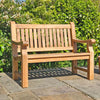 Wooden memorial bench on a stone patio with greenery in the background