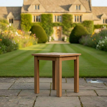 Wooden teak small garden table in a lush green garden with a house in the background