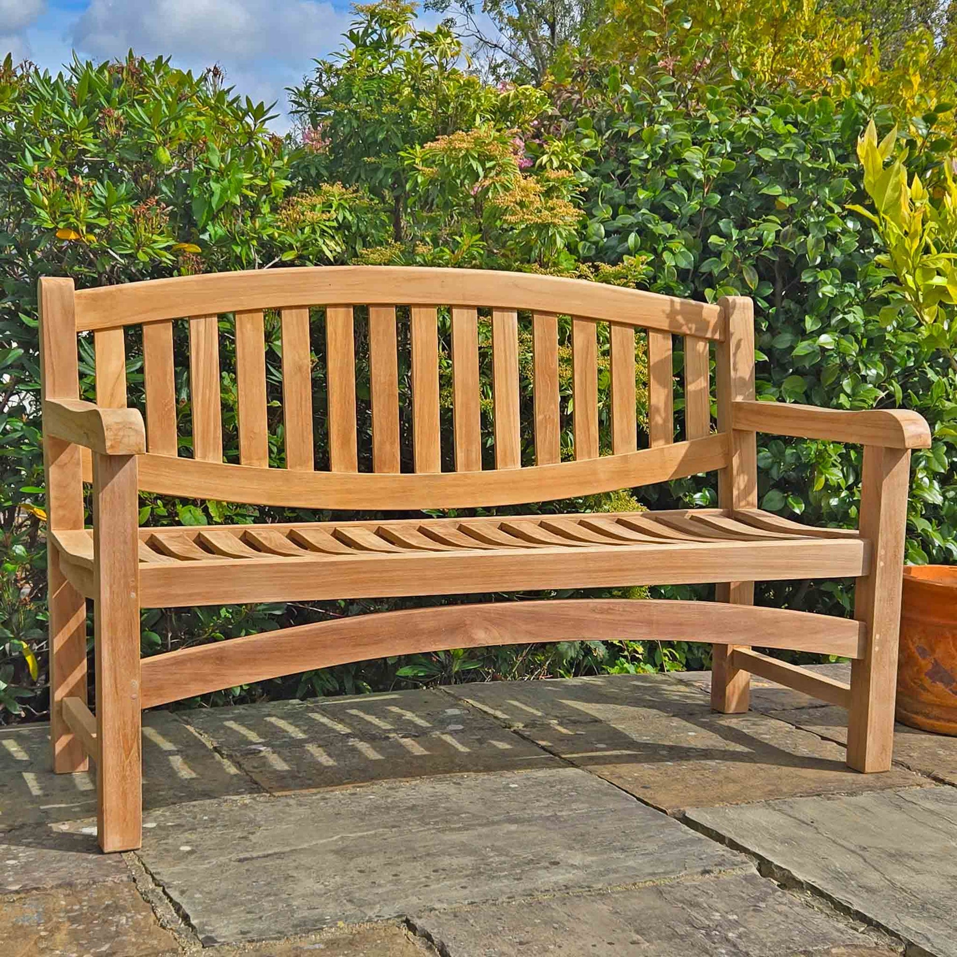 Wooden commemorative garden bench in a garden setting with greenery and a stone patio.